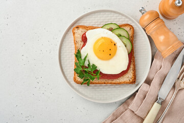 Toast with tomatoes ketchup, cucumber and fried egg on white plate, top view, grey background,
