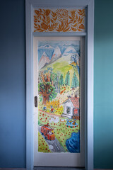 A wooden door painted by the artist with funny scenes from life. In the original interior of the house.
