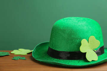 Leprechaun hat and decorative clover leaves on wooden table against green background, space for text. St Patrick's Day celebration