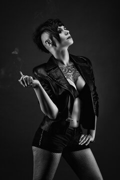 Attractive tattooed young woman, in profile, with punk hairstyle, wearing leather jacket, fishnet stockings, smoking a cigarette