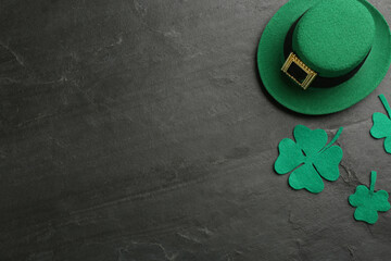 Leprechaun's hat and decorative clover leaves on black background, flat lay with space for text....