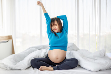 Pregnant asian woman stretching on the bed after wake up in the morning - Powered by Adobe