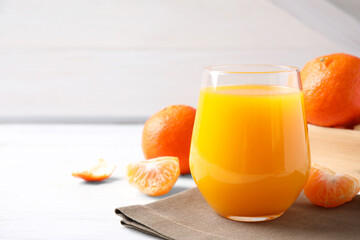Glass of fresh tangerine juice on white table, space for text