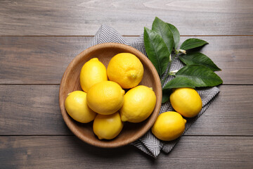 Many fresh ripe lemons with green leaves on wooden table, flat lay