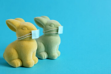 Cute bunny figures in protective masks on light blue background, space for text. Easter holiday during COVID-19 quarantine