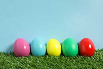 Fototapeta na wymiar Bright Easter eggs on green grass against light blue background