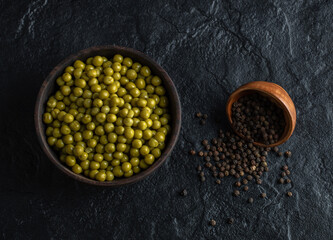 Close up view of white bowl full with green olives and black pepper seeds