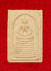 Macro Thai buddha amulet on the red velvet background.	

