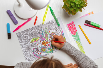 Woman paints coloring pages for adults on paper. Relaxing hobby.