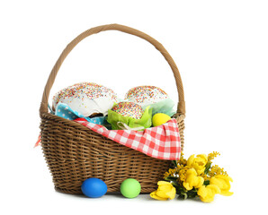 Basket with delicious Easter cakes, dyed eggs and flowers on white background