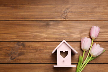 Beautiful bird house with heart shaped hole and tulips on wooden background, space for text. Spring flat lay composition