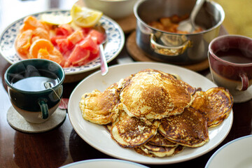 Brunch pancakes with citrus fruits, homemade apple jam and steaming, hot cup tea or coffee. 