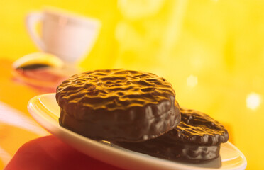 Chocolate chip cookies in a plate on a blurred yellow background and a coffee cup.