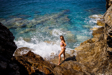 Young beautiful woman in a swimsuit stands on a rocky beach of the Mediterranean Sea. The concept of sea recreation. Selective focus