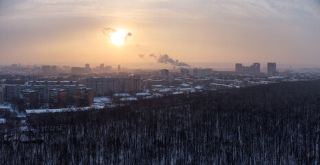 Aerial view Kharkiv city Pavlove Pole district. Smoke from pipes above winter dark forest, multistorey houses and snowy sunset sky