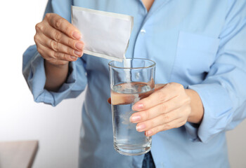 Woman pouring powder from medicine sachet into glass with water, closeup