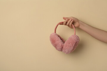 Woman holding stylish winter earmuffs on beige background, closeup. Space for text