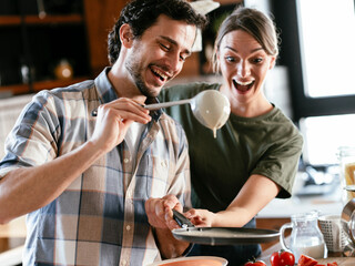 Young couple having fun while preparing food. Boyfriend and girlfriend making pancakes at home.