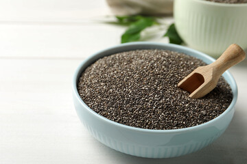 Bowl with chia seeds and wooden scoop on white table. Space for text