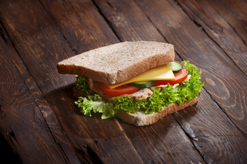 bacon sandwich closeup with fresh tomatoes, lettuce salad leaves, cucumber and cheese, on wooden rustic table background