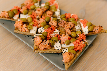 Delicious spicy tomato Italian snacks, or bruschetta, on slices of toasted baguette, decorated with basil, red fish, ham on a wooden board