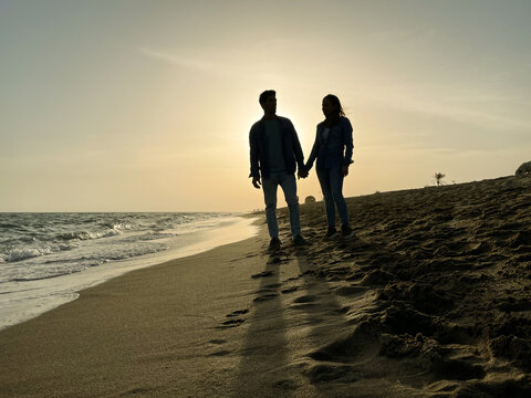 Backlit young couple on the beach at sunset.