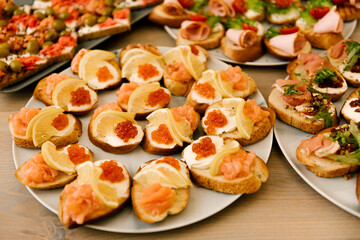 Delicious spicy tomato Italian snacks, or bruschetta, on slices of toasted baguette, decorated with basil, red fish, ham on a wooden board