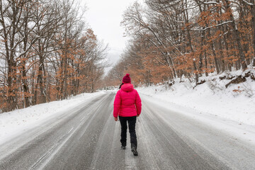 Woman walks on the white road in the snowy forest.
