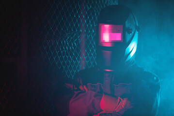 Welder in the neon lights in the welding helmet.