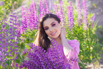 Summer portrait of attractive young woman with purple lupin flowers outdoors