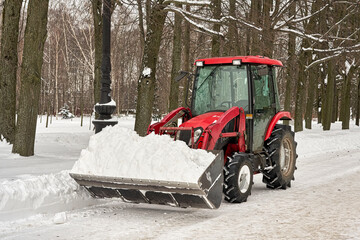 Red tractor with a bucket of praying snow cleans the park