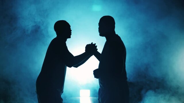 Two sportsmen are shaking hands in a room filled with smoke
