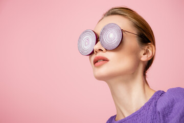 young woman posing in eyeglasses with purple onion rings isolated on pink, surrealism concept