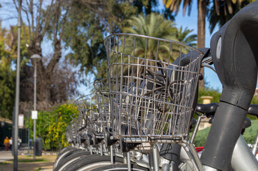 Numerous bicycles parked at a shared bike service station. Close up view of a bicycle with a metal basket. Bicycles parked on the street on a sunny day.