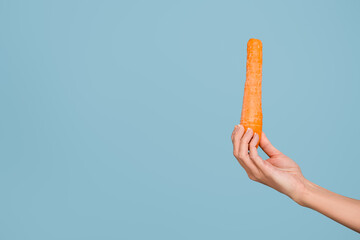 female hand with fresh whole carrot isolated on blue