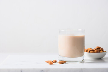 Almond milk in glass and nuts on white background. Close up. Lack of cholesterol. Copy space.