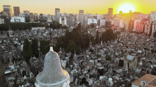 Aerial shot flying beside church bell tower towards La Recoleta cemetery at sunset