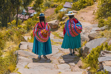 Two Peruvian indigenous Quechua women walking along a trail in traditional clothing and textile...