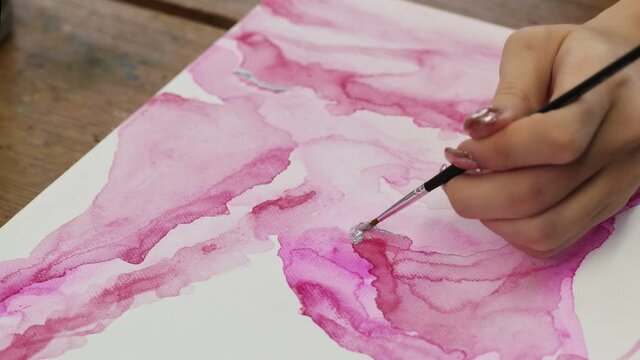 Fluid Art. Abstract pink painting. Close up of female artist uses paintbrush and silver paint to draw an abstract picture