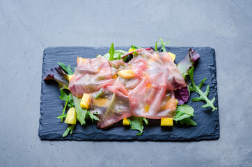 Healthy and colorful salad with sliced fish carpaccio, lattuce, and ananas