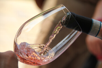 Rose wine being poured into a glass during an outdoor party.