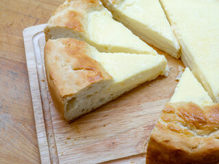 Close-up of triangular slices of sour cream pie - a national Tatar dish. A huge homemade cheesecake with toasted edges and tender filling on a wooden table.