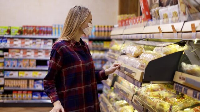 Young woman carries a cart in the supermarket taking bread