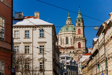 Fototapeta na wymiar View of Baroque Church of Saint Nicholas, green dome and bell tower with clock, sunny winter day, snow on red roofs, Mala Strana or Lesser Town district, Prague, Czech Republic