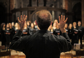 Musician leads a choir during a concert in a cathedral. Musical rehearsals before the concert during the Christmas period. Life of musicians and classic holy music. - obrazy, fototapety, plakaty