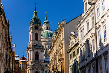 Fototapeta na wymiar View of Baroque Church of Saint Nicholas, green dome and bell tower with clock, sunny winter day, snow on red roofs, Mala Strana or Lesser Town district, Prague, Czech Republic