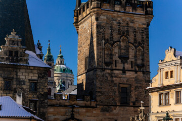 Medieval ancient Charles Bridge landmark looking toward Lesser Town with gothic stone bridge tower, Baroque Church of Saint Nicholas, snow, sunny winter day, Prague, Czech Republic