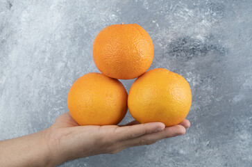 Male hand holding three oranges on marble background