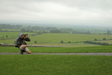 Crouched professional photographer takes a photo. Adventurous tourist fascinated by the green...