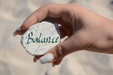 hand holding a white stone with the inscription "balance"